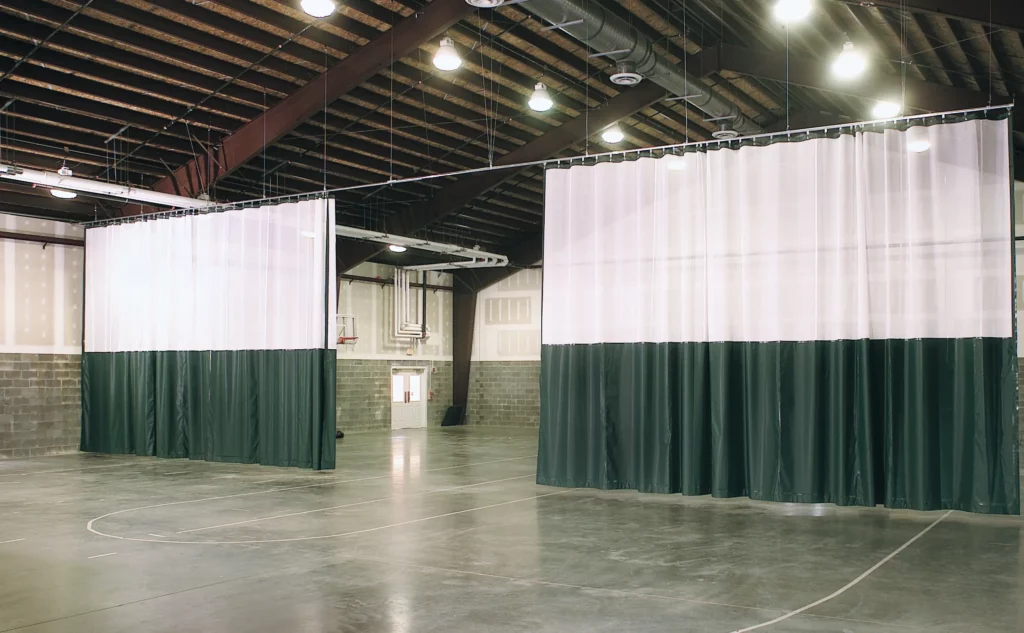 Green and white handing gym divider separates basketball courts.