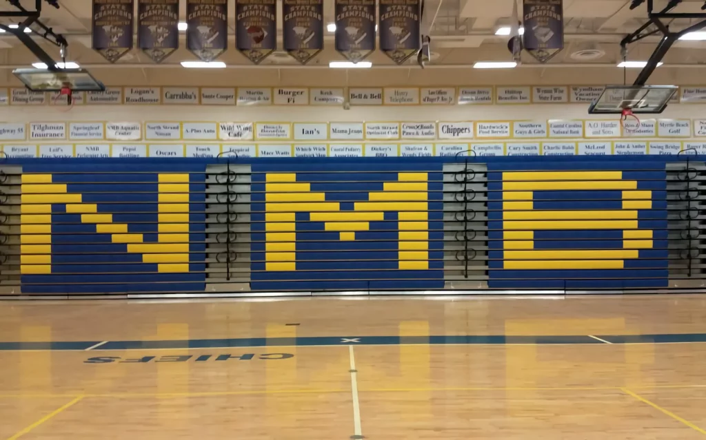 Blue indoor telescopic bleachers are retracted in a gym.