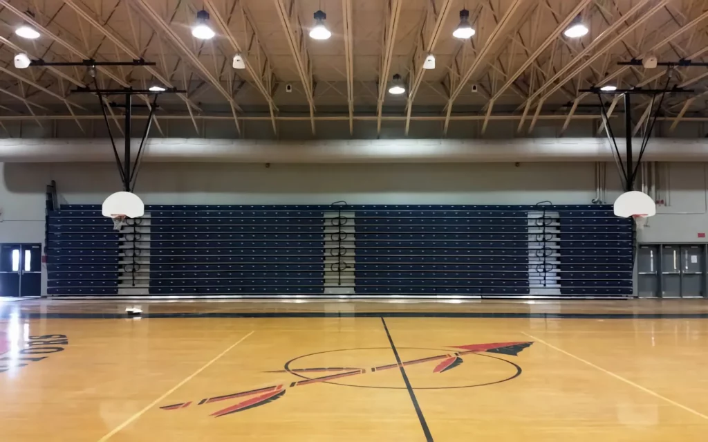 Blue telescopic bleachers are retracted and stored in a gym.
