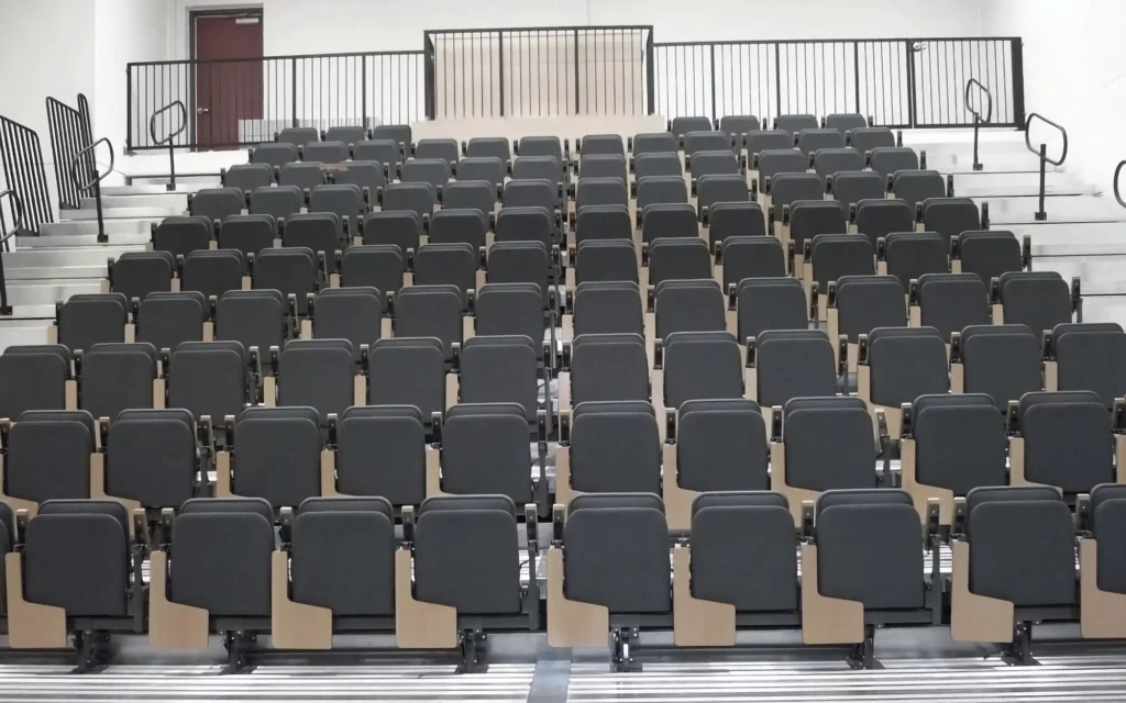 A theater platform is shown installed with padded gray seats and attached wood-finished desks.
