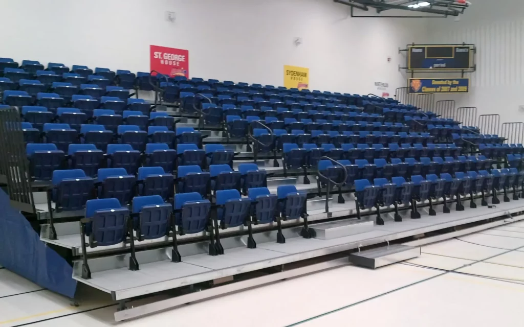 A blue theater platform is shown installed in a gym.